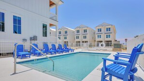Une piscine avec des chaises bleues et un bâtiment blanc en arrière-plan.