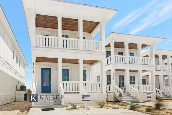 Un immeuble de deux étages avec une porte bleue, des balustrades blanches et une pancarte indiquant qu’il est à louer.