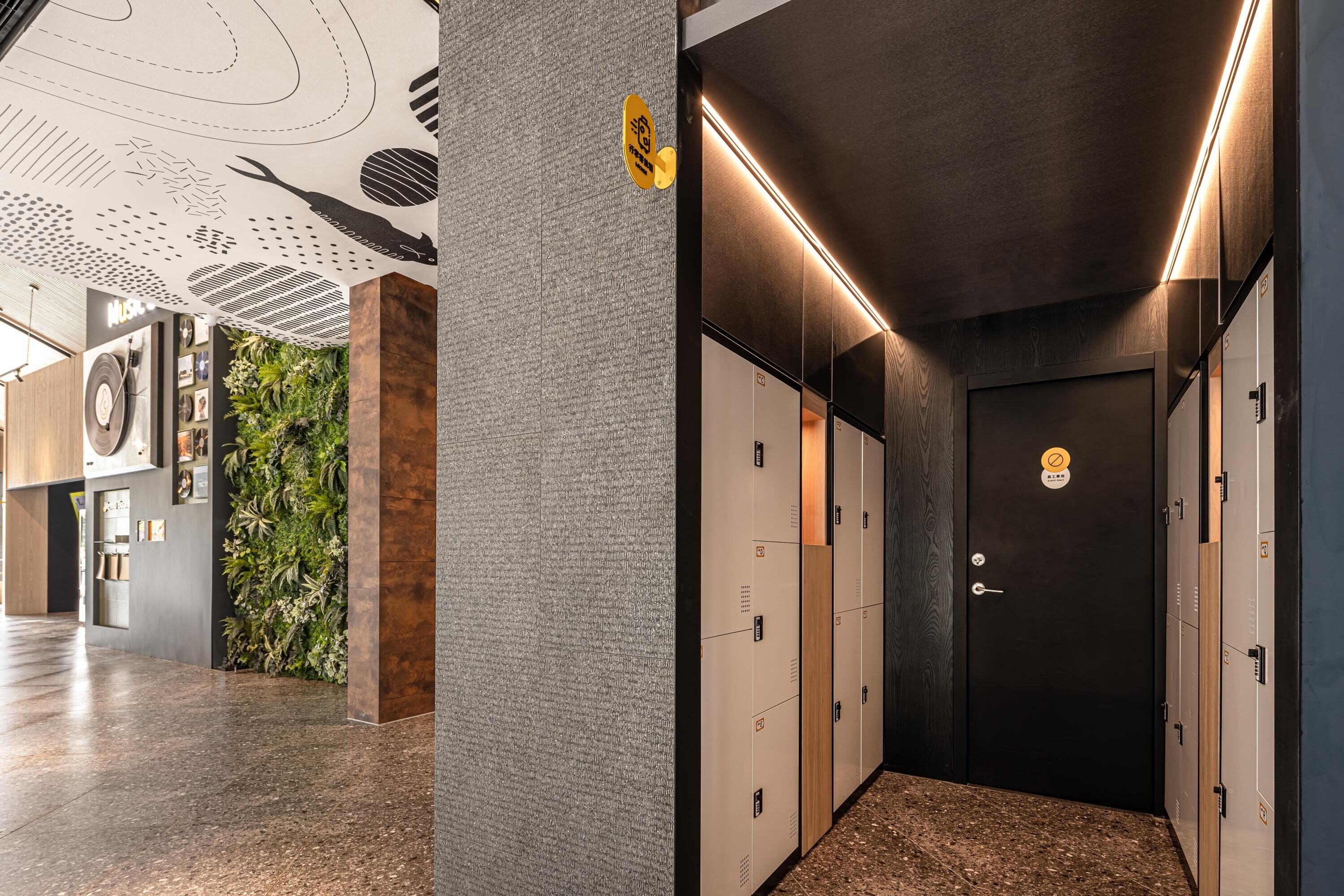 A modern hotel lobby with lockers, a reception desk, and a wall with a vertical garden.