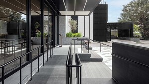 A modern outdoor area with glass railings, a covered walkway, and a seating area with plants. - The Moment Hotel Hualien by Lakeshore (Xincheng)