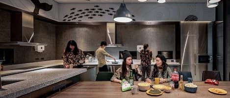 A modern kitchen with a wooden dining table, various food items, and people engaged in conversation.