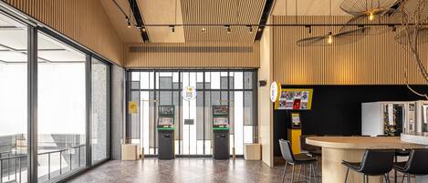 A modern interior with a large glass door entrance, vending machines, a wooden bar area, and a seating space with chairs.