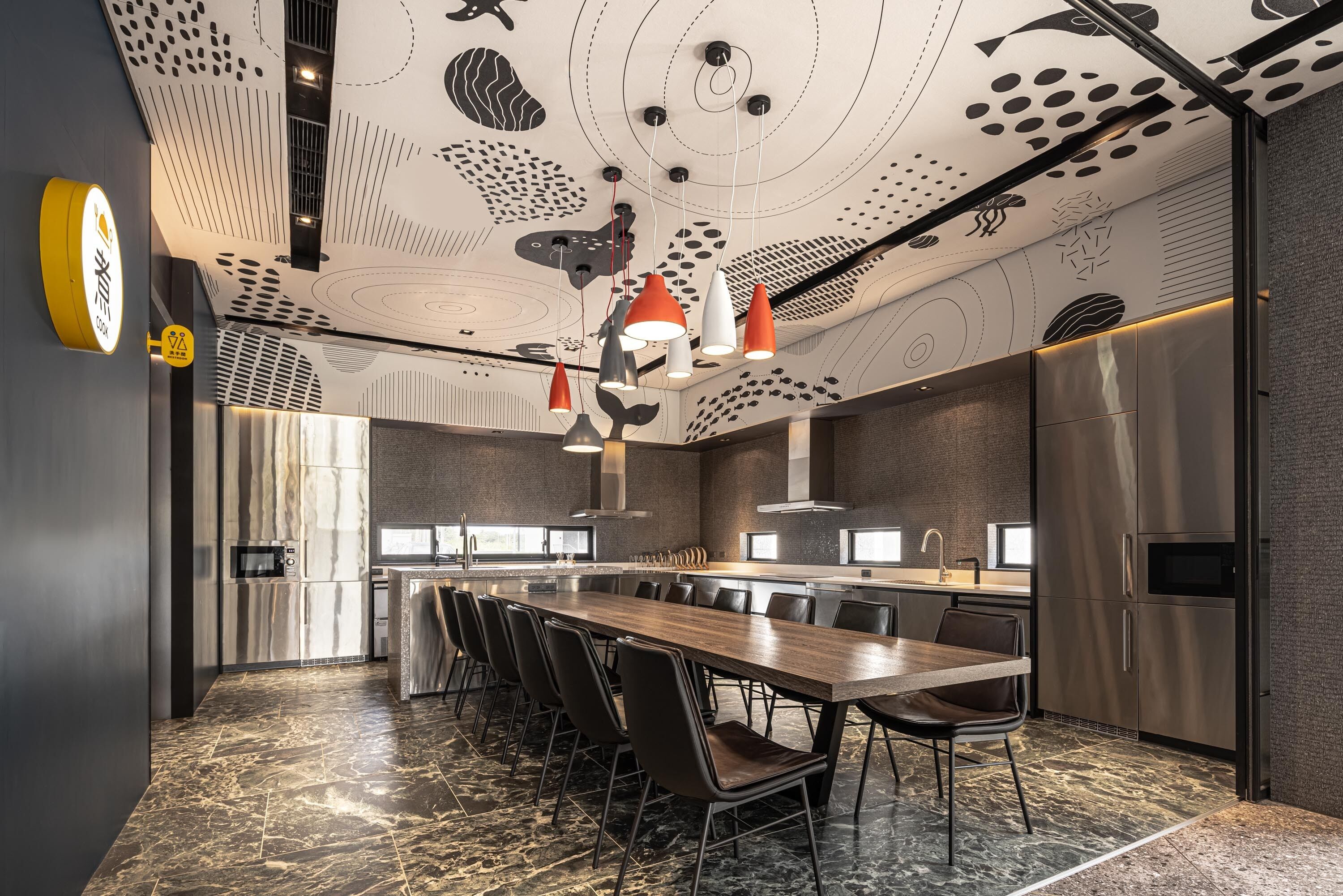A modern kitchen with a long island, stainless steel appliances, and a marble floor.