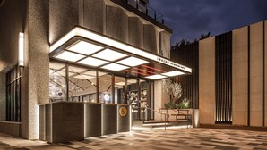 A modern hotel entrance with a glass facade, a reception desk, and a staircase leading to the entrance. - The Moment Hotel Hualien by Lakeshore (Xincheng)