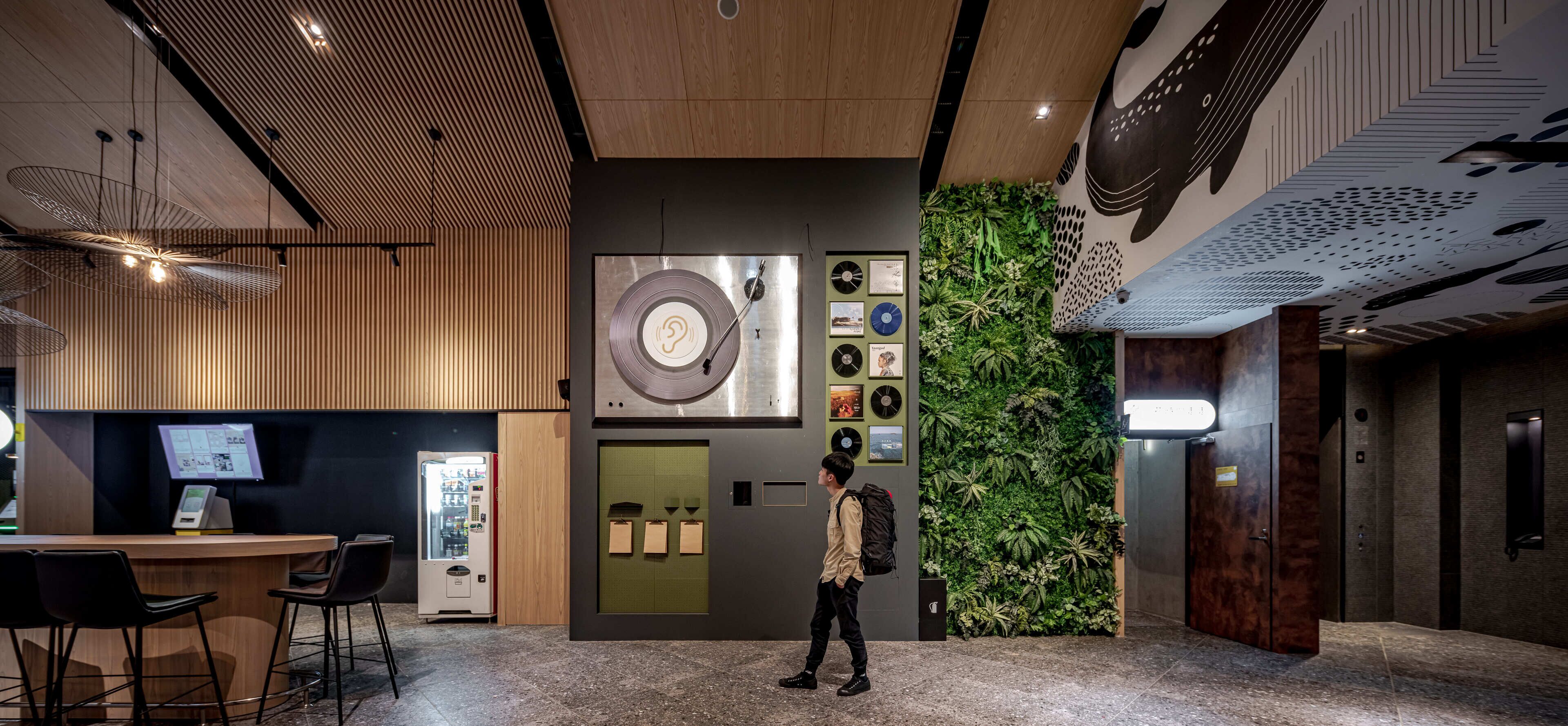 Un hall d’entrée moderne avec un comptoir d’accueil en bois, un distributeur automatique, un mur orné d’un motif circulaire et un jardin vertical.