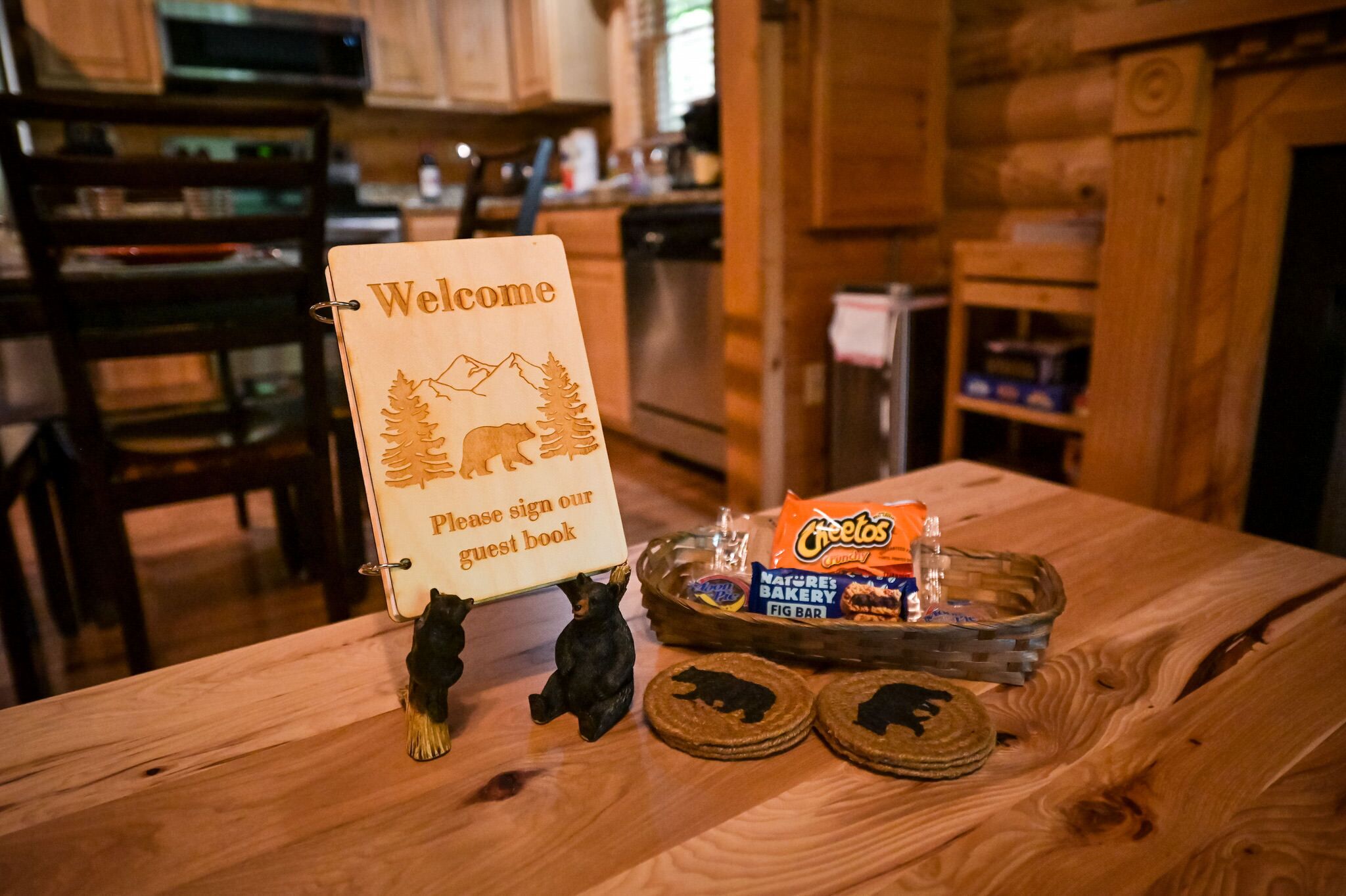 A wooden table with a welcome sign, a basket of snacks, and two coasters.