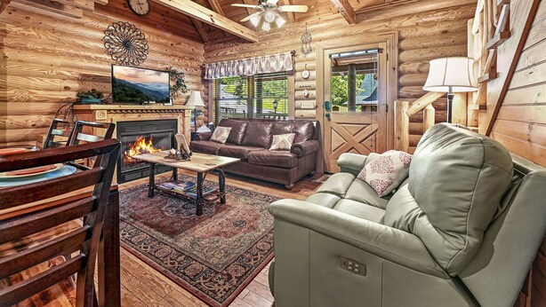 Ein Blockhaus-Interieur mit Kamin, Ledersofa, Esstisch aus Holz und einem Fernseher.