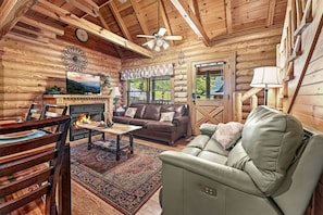 A log cabin interior with a fireplace, leather sofa, wooden dining table, and a television.