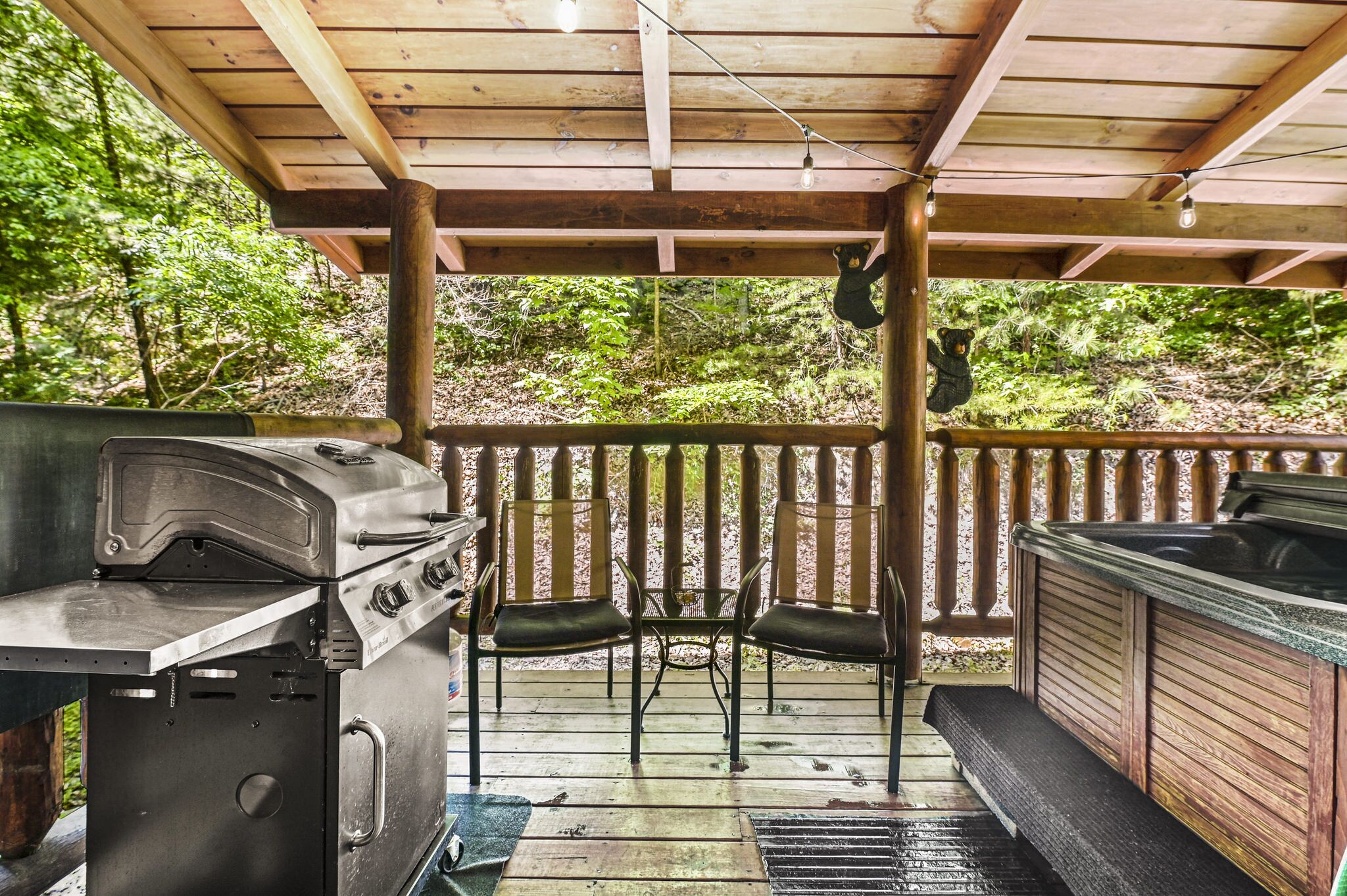 A covered outdoor patio with a grill, two chairs, and a hot tub.