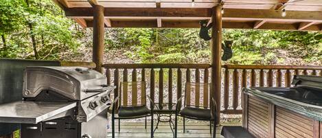 A covered outdoor patio with a grill, two chairs, and a hot tub.