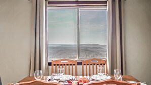 A dining table set for four with chairs, a window with a view of a landscape, and three hanging light fixtures. - Summit 304B  3 Bedrooms 2 Full Baths (Snowshoe)