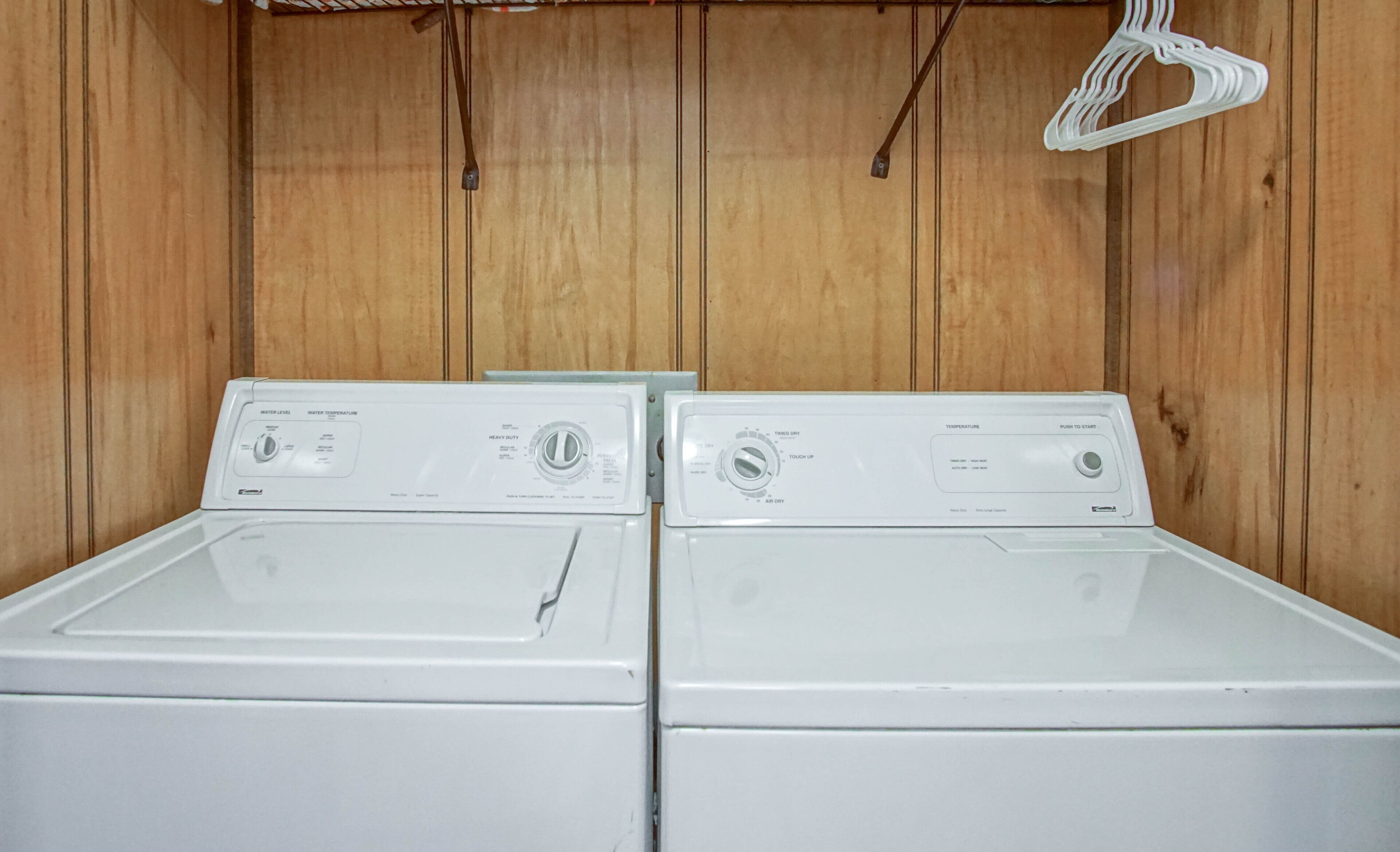 Two front-loading washing machines in a wooden-walled laundry room with a metal rack above.