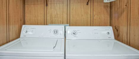 Two front-loading washing machines in a wooden-walled laundry room with a metal rack above.