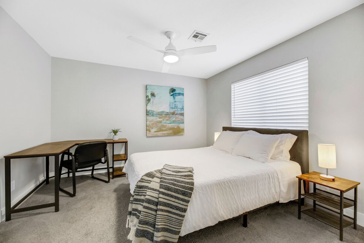 Une chambre à coucher comprenant un lit, un bureau, une chaise et un ventilateur de plafond.
