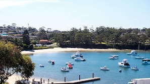 A marina with several boats docked, a sandy beach, and a backdrop of residential buildings and trees.