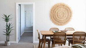 Un coin repas avec une table en bois et des chaises en osier, une décoration murale tissée et une plante en pot.