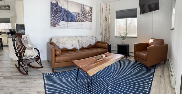 A modern living room with a brown leather sofa, a wooden coffee table, and a blue patterned rug. - DENALI PENTHOUSE, lakefront near Talkeetna and Denali State Park (Trapper Creek)