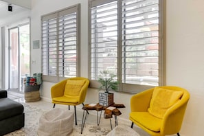 Relax in a serene space with a seating area, featuring two armchairs and a multi-tiered table, amidst lush greenery and a patterned rug.