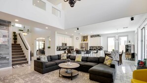 A spacious living area with a sectional sofa, a coffee table, and a yellow chair. A staircase with a wooden railing leads to an upper level. - Modern Gem w/ Fire Pit: 3 Mi to Goodyear Ballpark! (Goodyear)