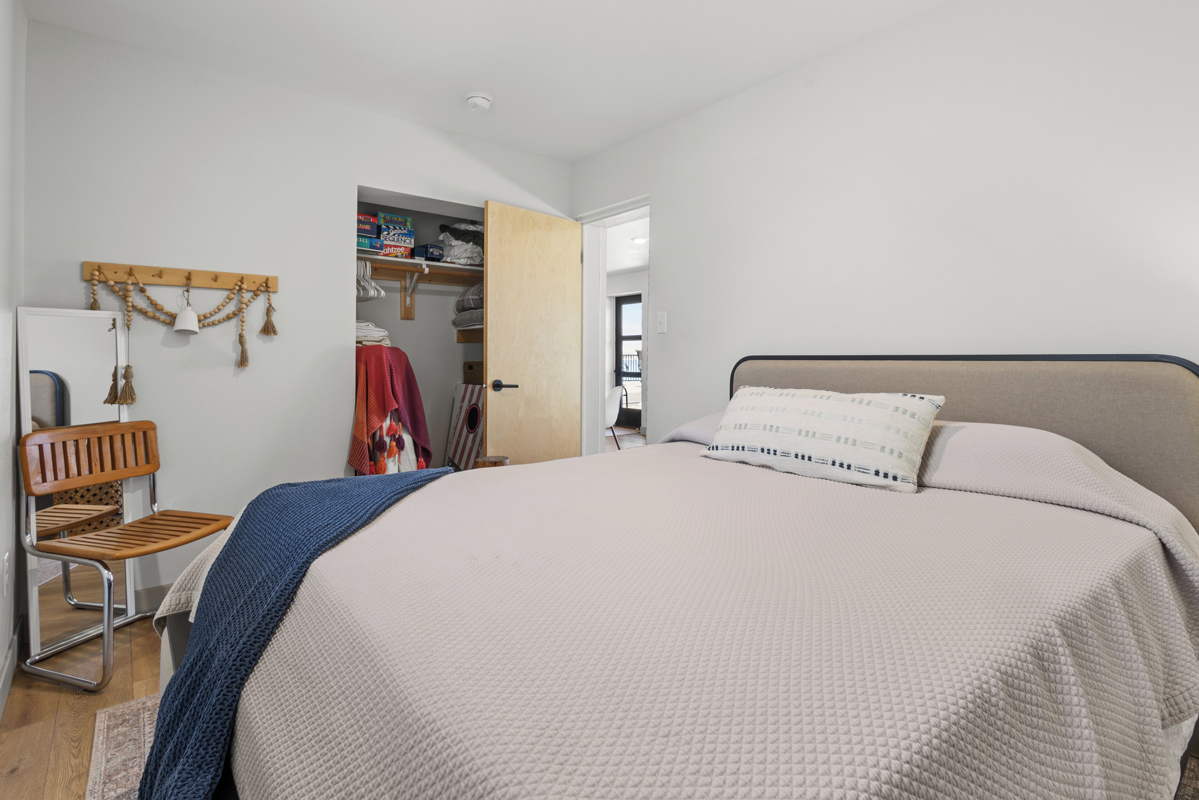 Un dormitorio con cama, una silla, un armario y una puerta que da a otra habitación.