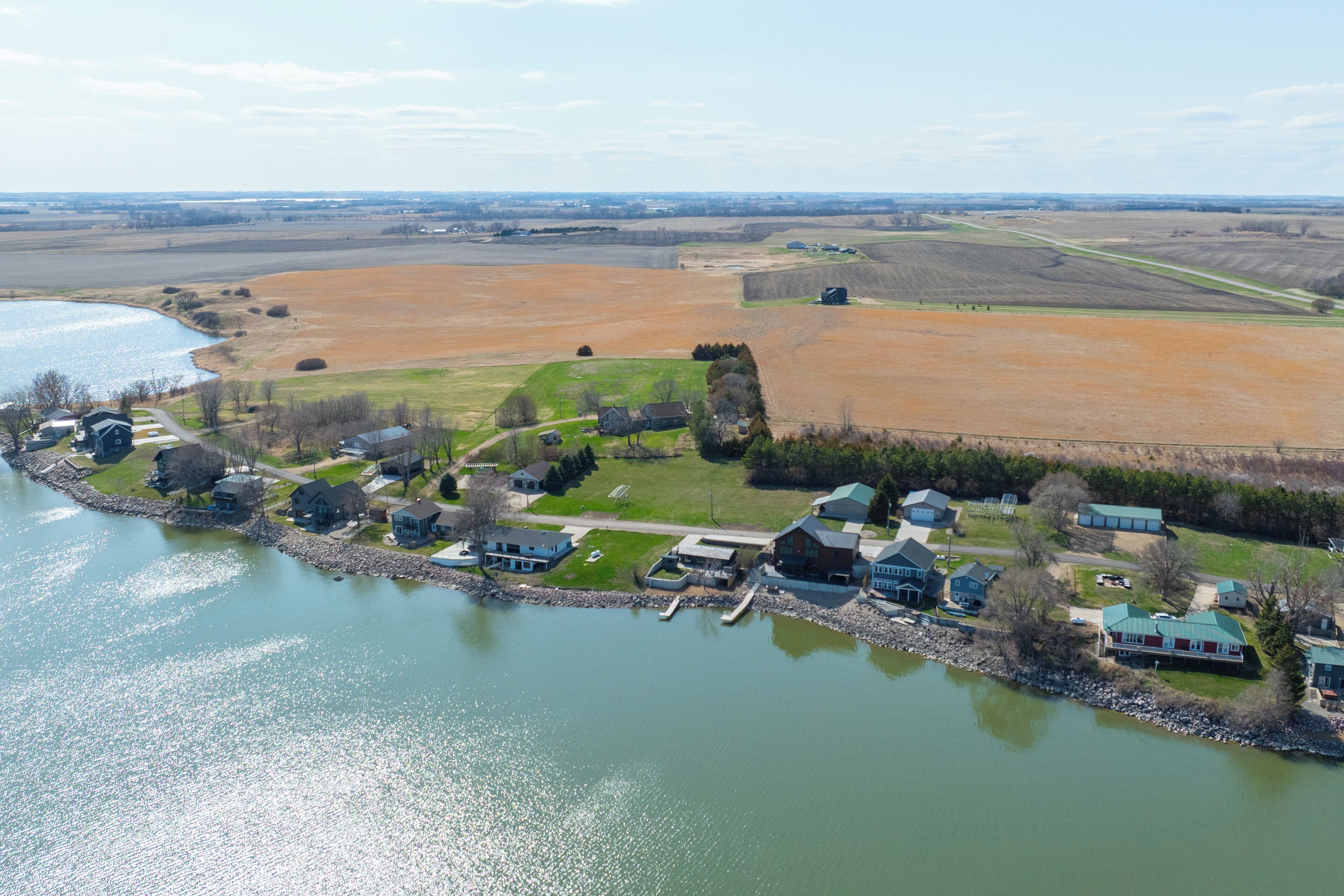 Vista aérea de una propiedad junto al lago con casas, un muelle y campos circundantes.