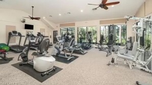 Een ruime fitnessruimte met diverse trainingsapparaten, plafondventilatoren en grote ramen.