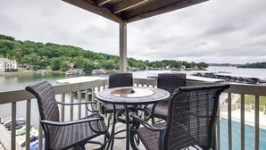 Un balcón con sillas de mimbre y una mesa, con vista a un lago con barcos y muelles.