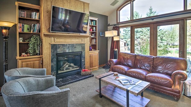 A living room with a fireplace, a television, a leather couch, and a bookshelf. - Large Home w/ Patio & Yard, 2 Mi to Downtown (Bozeman)