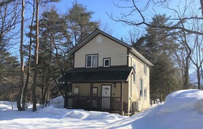 A two-story house with a porch, surrounded by snow and trees.