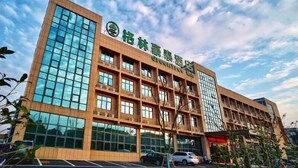 A multi-story hotel with a modern architectural design, featuring large glass windows and a prominent green logo on the facade. - Greentree Inn Changzhou Jintan District Xerbu Town East Salt Lake City Business Hotel (Changzhou)