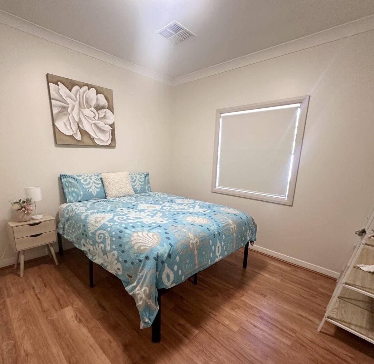 A bedroom with a bed, a nightstand, a window, and a wall-mounted artwork.