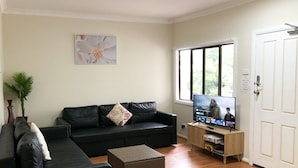 A living room with a black sofa, a television, a wooden cabinet, and a door. - Charlestown Central 5 Bedrooms Front House (Charlestown)