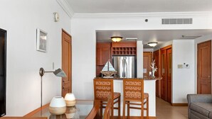 Una sala moderna con una mesa de comedor de vidrio, sillas de madera, un sofá y una zona de cocina con armarios de madera y un refrigerador de acero inoxidable.