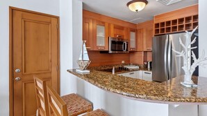 Una cocina con gabinetes de madera, encimera de granito, refrigerador de acero inoxidable y microondas.