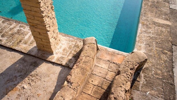 A stone pool with clear blue water, surrounded by stone walls and steps leading down to the pool.