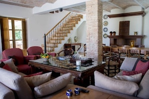 A spacious living room with a staircase, red upholstered chairs, a glass coffee table, and a dining area with wooden chairs. - Villa "Luz Casa Valenciana Siglo XIX" with Mountain View, Pool & Wi-Fi (Corbera)
