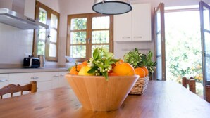 A kitchen with a wooden table, a bowl of fruit, and a hanging light fixture.