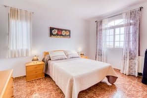 Une chambre à coucher avec un lit, des tables de chevet, une lampe, un tableau et une fenêtre avec des rideaux.