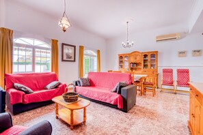 Un salon avec un canapé rouge, une table basse en bois et un coin repas comprenant un buffet en bois et des chaises.