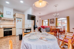 Un coin repas avec une table dressée pour quatre personnes, une cuisine équipée d’un réfrigérateur, d’un four et d’un téléviseur fixé au mur.