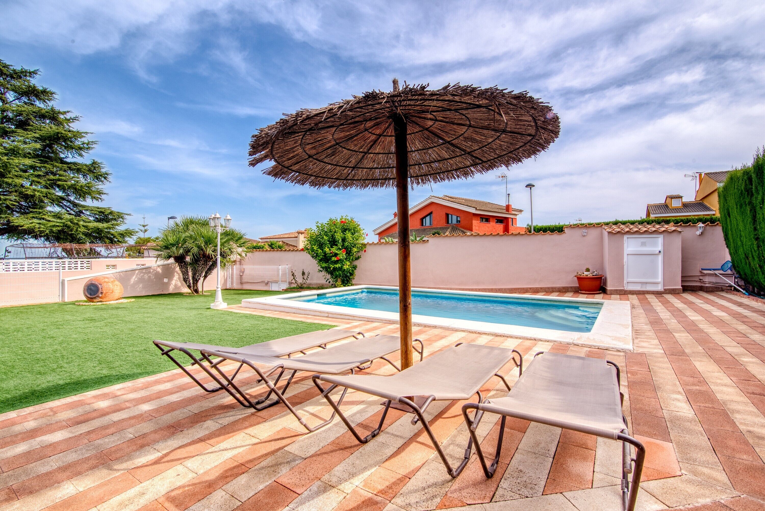 A swimming pool with lounge chairs and an umbrella, surrounded by a brick patio and a green lawn.