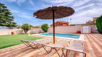 A swimming pool with lounge chairs and an umbrella, surrounded by a brick patio and a green lawn.