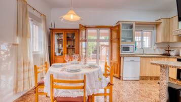 Un comedor con una mesa dispuesta para cuatro, sillas de madera, un armario con puertas de vidrio, un microondas y un lavavajillas.