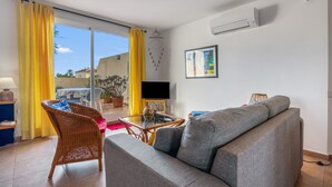 Een woonkamer met een bank, een rieten stoel, een glazen tafel en een televisie.
