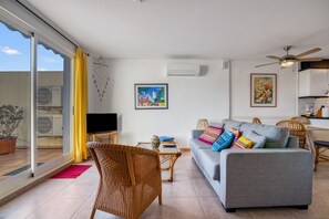 A living room with a sofa, a television, a ceiling fan, and a dining area with chairs.