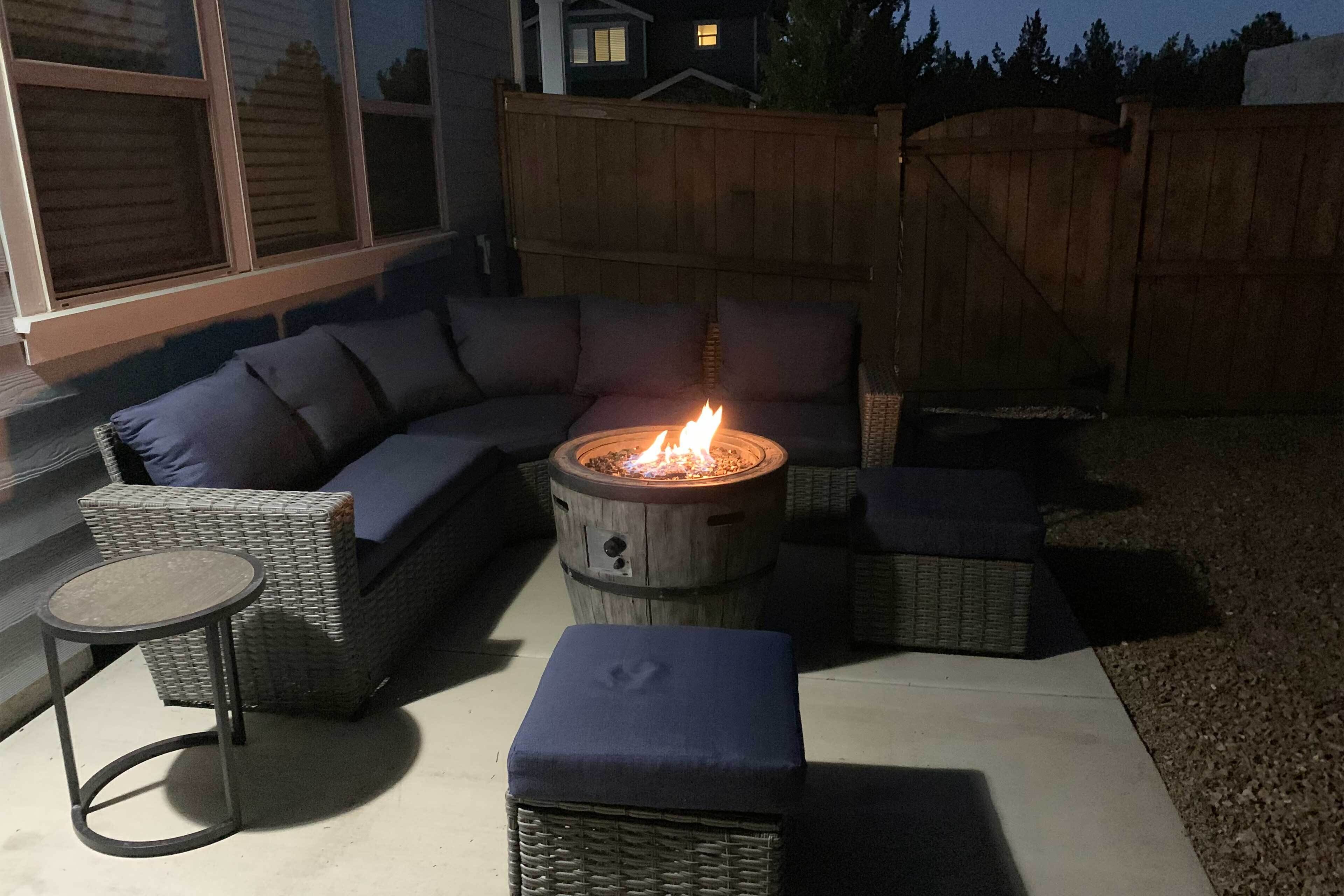 En terrasse med bålsted, fletningsmøbler og udsigt til huset.