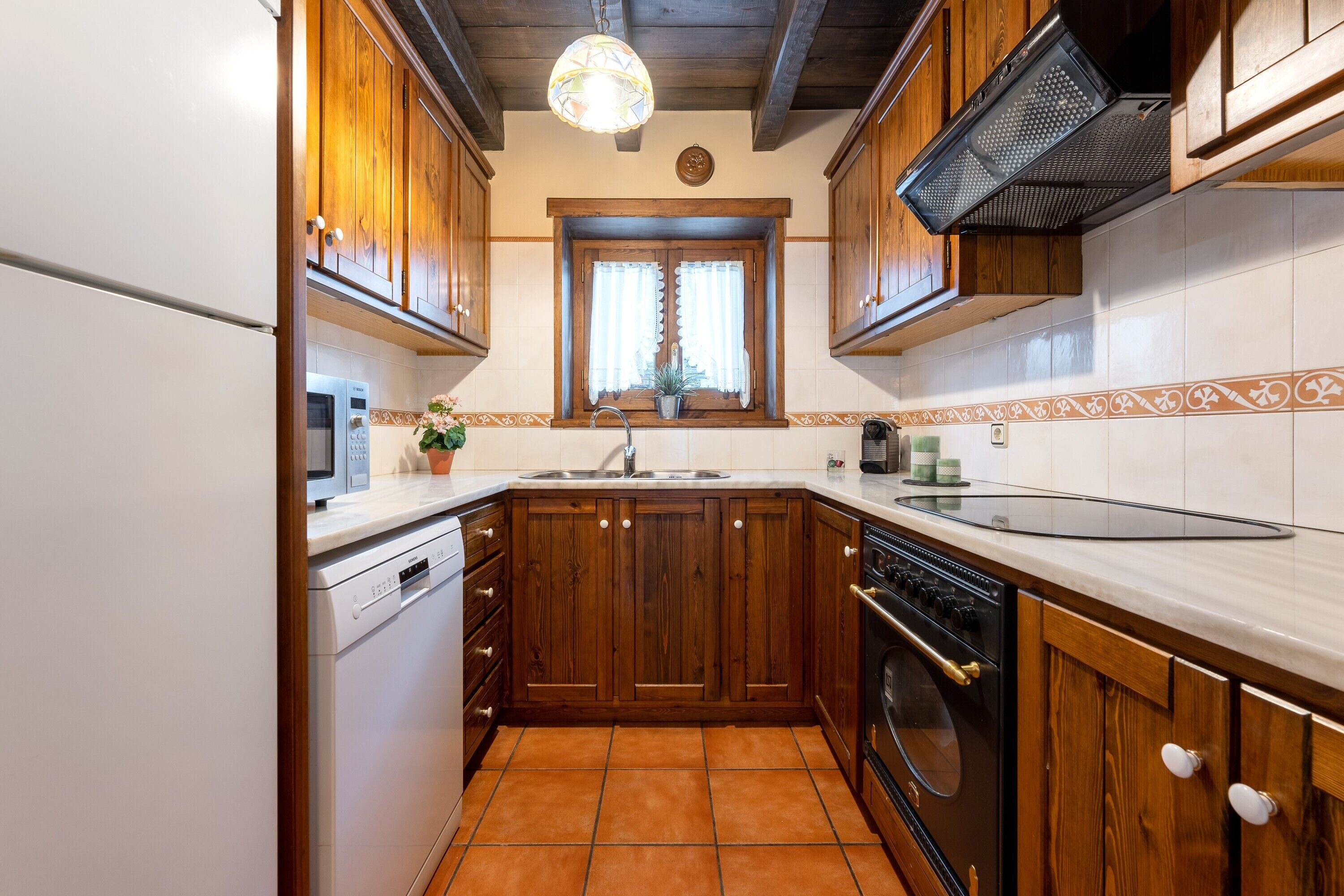 A kitchen with wooden cabinets, a built-in oven, a dishwasher, and a window with curtains.