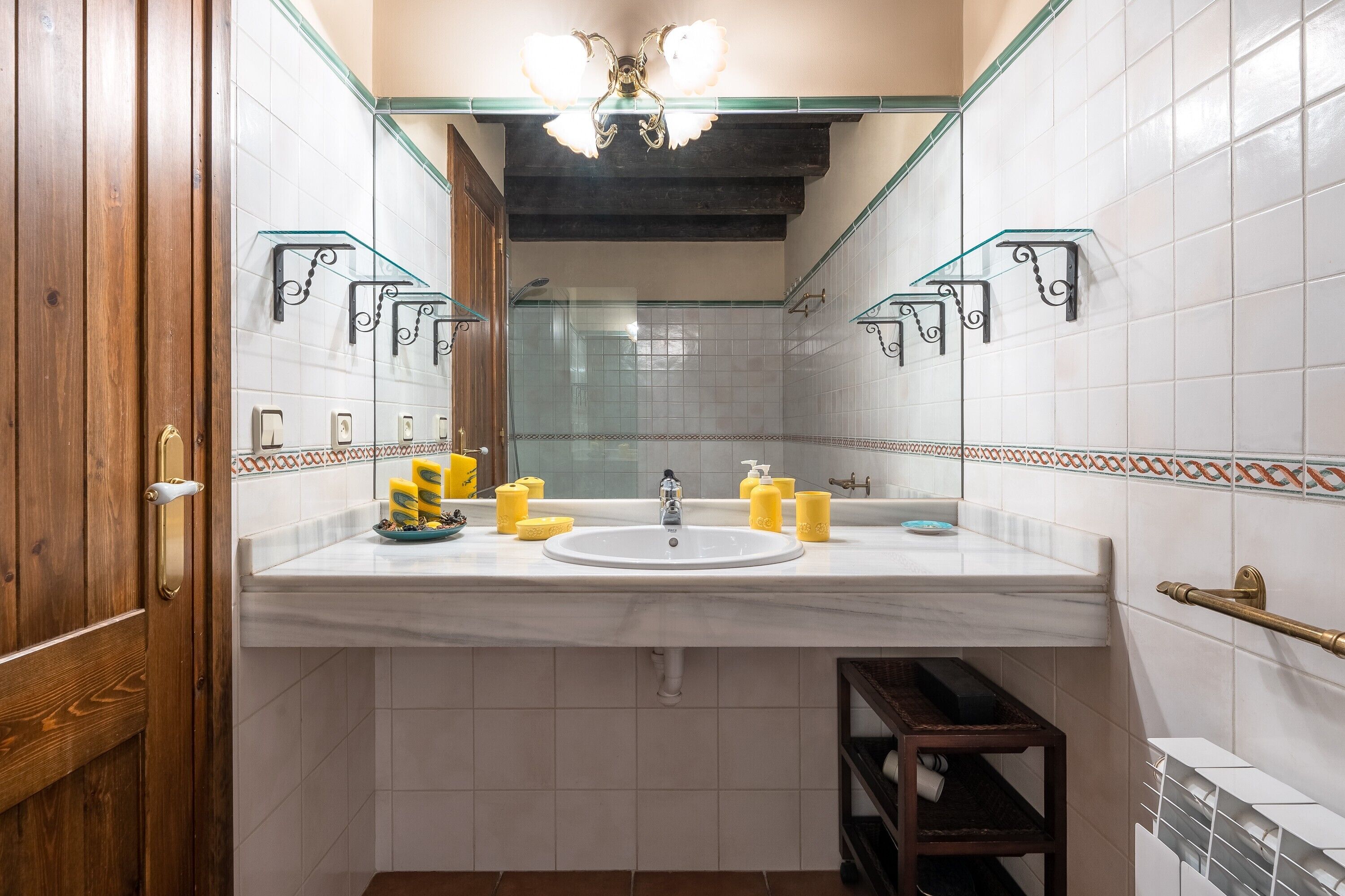 Une salle de bain avec un lavabo blanc, des articles de toilette jaunes, une cabine de douche en verre et une porte en bois.