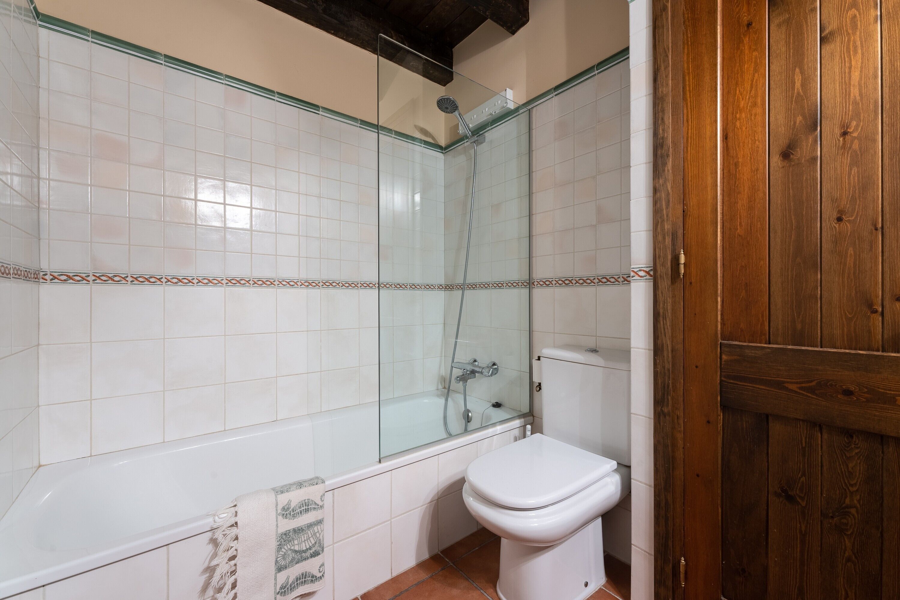 Casa de banho com chuveiro envolto em vidro, sanita branca e porta de madeira.