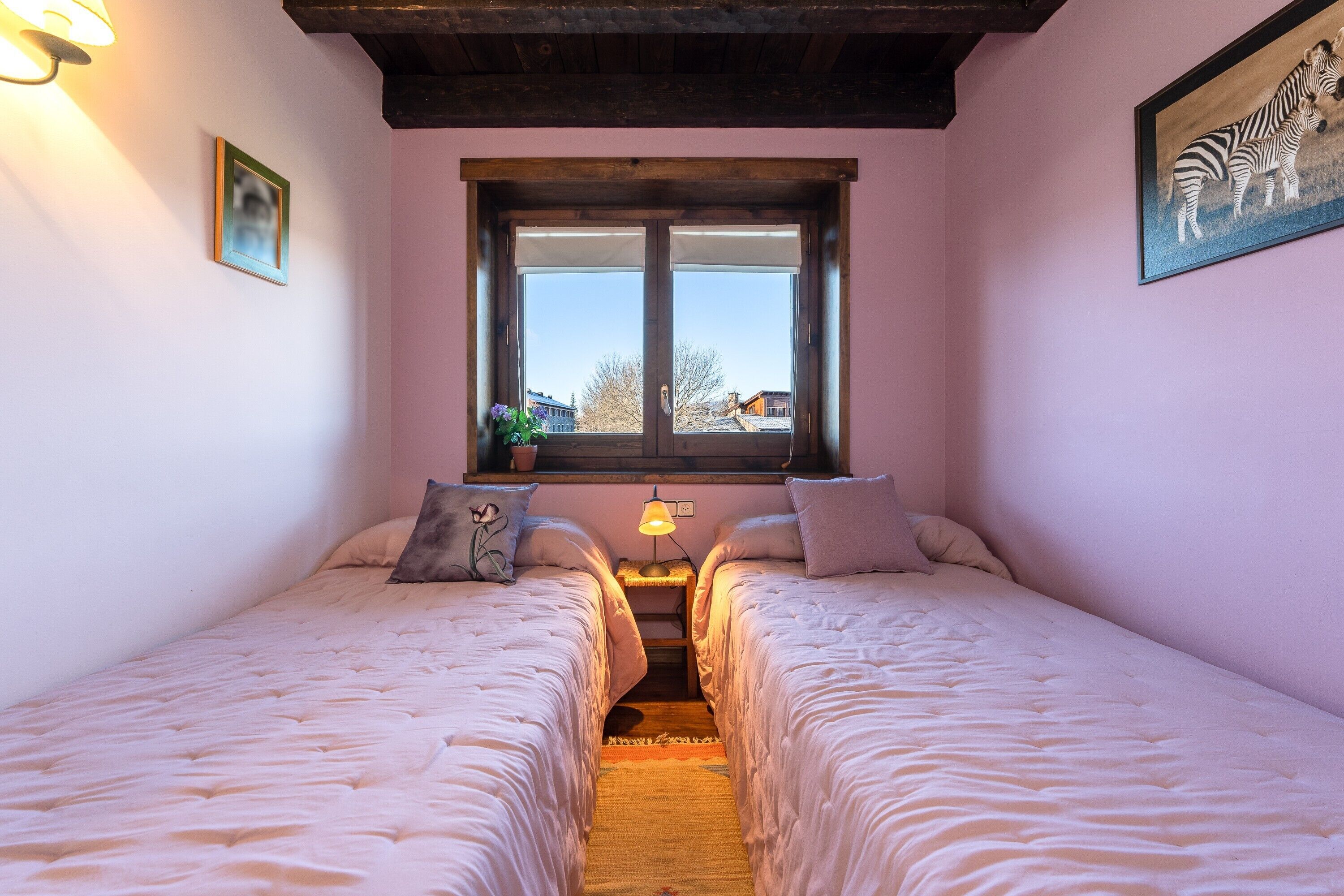 Een slaapkamer met twee bedden, een raam met uitzicht, een lamp en een lijst met een afbeelding aan de muur.